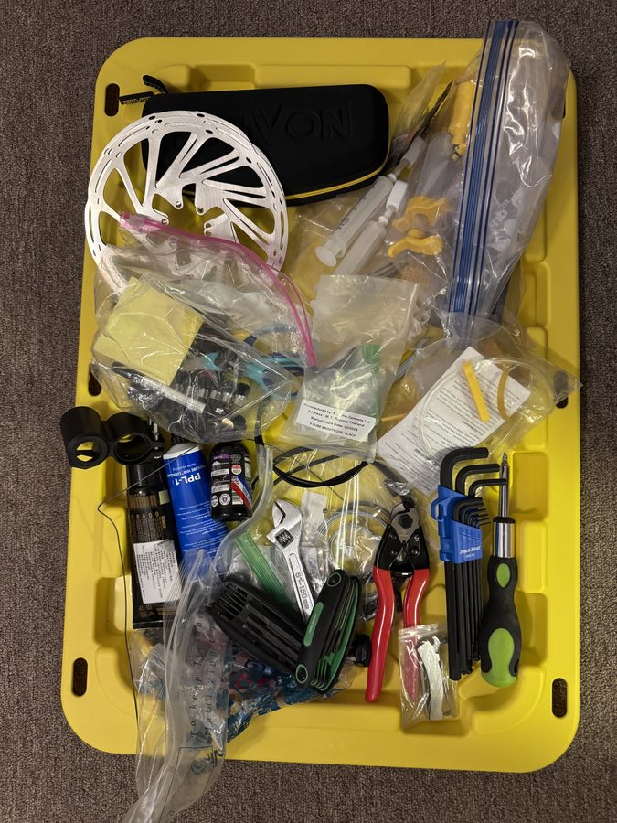A tool tray of bike gear: hex keys, cable cutters, screwdrivers, a brake rotor, bleed kit and bagged spares