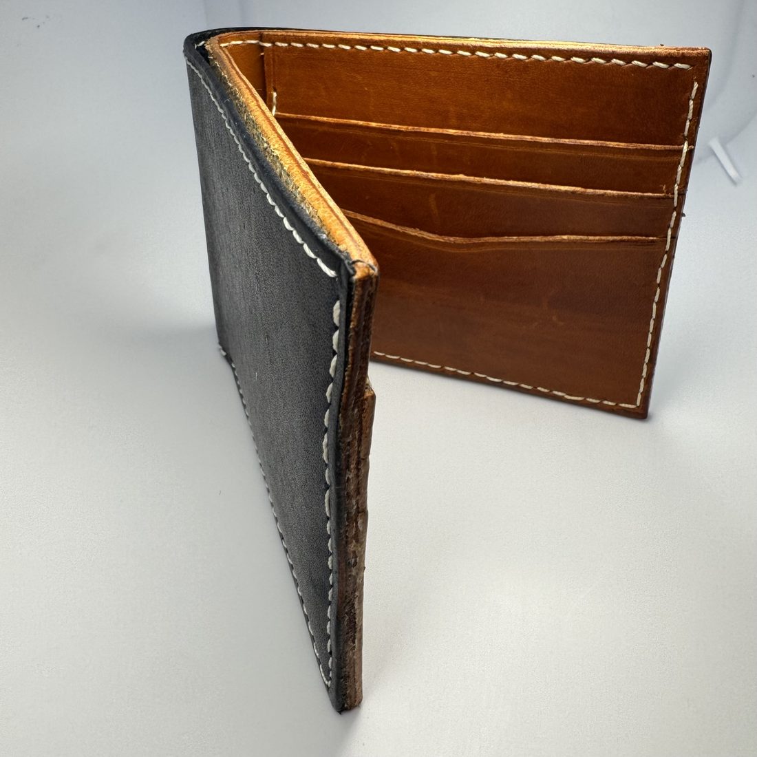 The first wallet, standing open: dark scuffed outer leather, uneven white stitching and rough unburnished edges