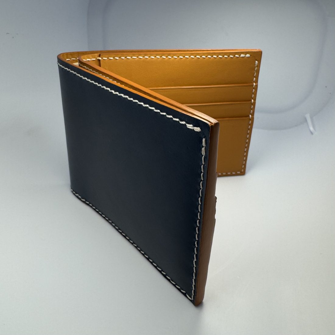 The second wallet in the same pose: navy outer leather with a tan interior, regular white saddle stitching and clean burnished edges